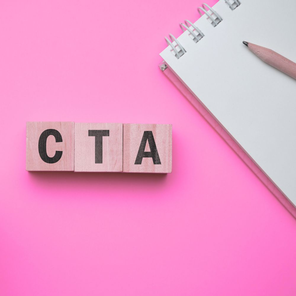 Call to action (1) CTA on wooden blocks on pink background with notepad and pen one of the website mistakes