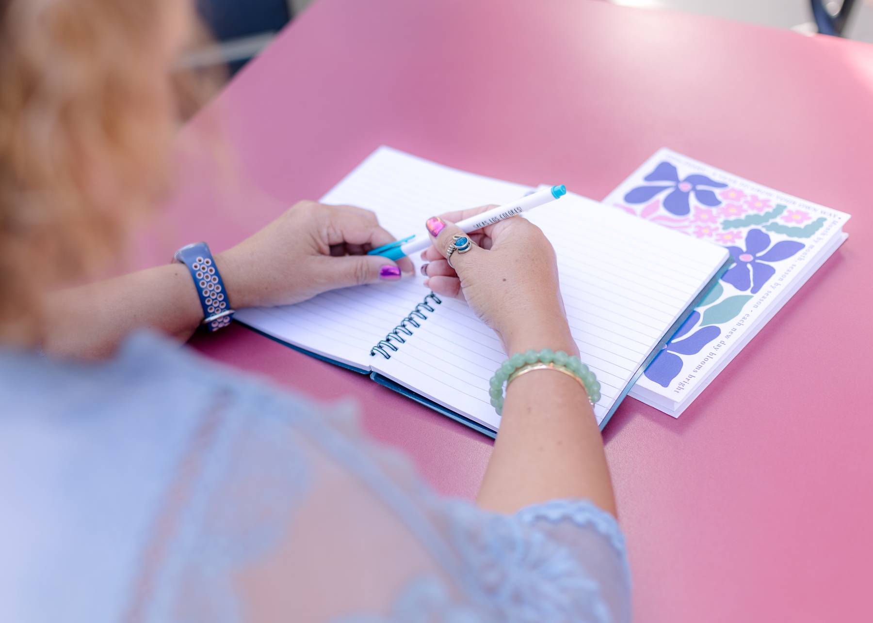 Woman writing in a notebook on a pink desk while planning business tasks in a calm, focused way best for ADHD Business Owners